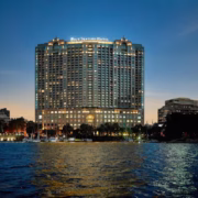 The Four Seasons Hotel Cairo at Nile Plaza illuminated at twilight, overlooking the Nile River with boats in the foreground.